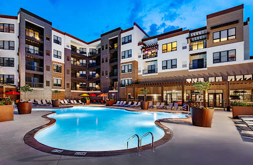 A large swimming pool is surrounded by a patio area with chairs and umbrellas.