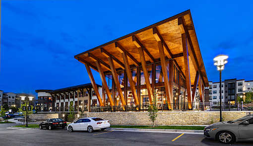 A modern building with a wooden facade is illuminated at dusk with cars parked in front.