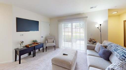 A living room with a grey couch, a coffee table, a flat screen TV, and a window with blinds.