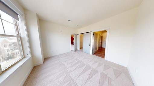 A large, empty room with a carpeted floor and a window on the left side.