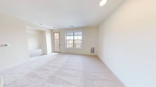 A large, empty room with a carpeted floor and a window with blinds.