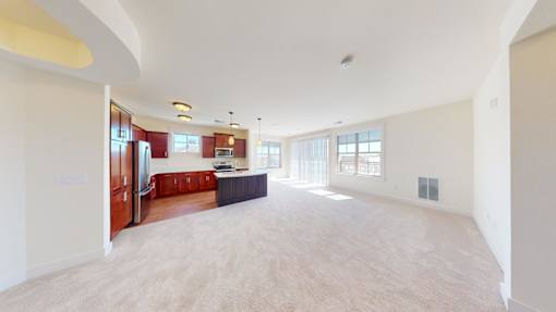 A spacious living room with a kitchen area in the background.