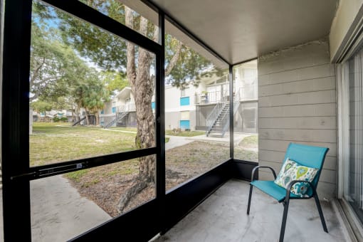 screened in porch with blue chair and large windows overlooking the yard