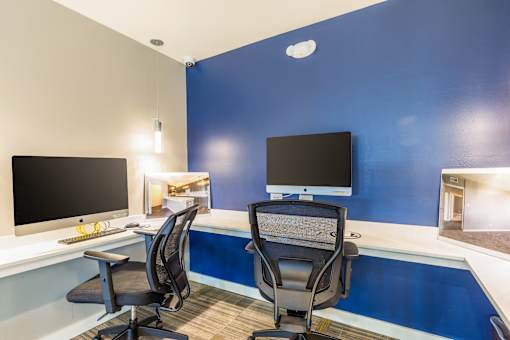 Two black computer monitors on a desk with two chairs.