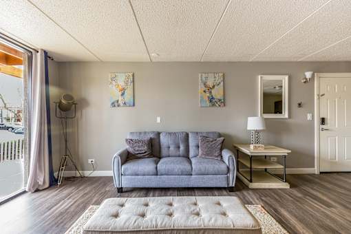 A grey couch sits in a living room with a lamp and two pictures on the wall.