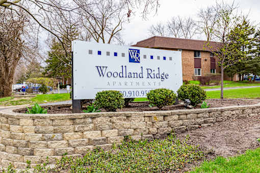 A sign for Woodland Ridge Apartments stands in front of a brick building.
