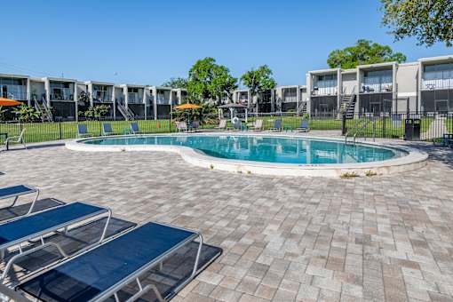 A round swimming pool surrounded by a brick patio and lounge chairs.