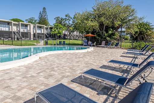 A pool surrounded by chairs and trees.