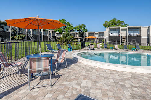 A pool area with a table and chairs and an orange umbrella.