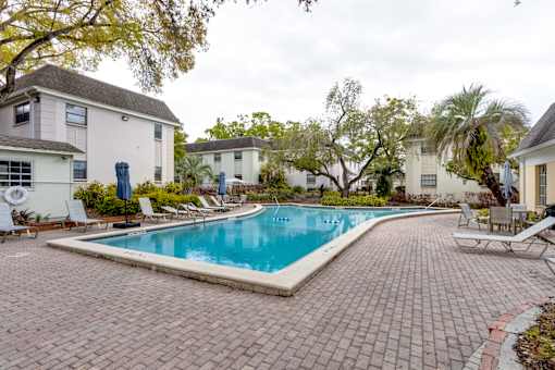 A swimming pool surrounded by a brick patio and lounge chairs.