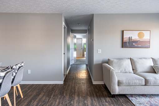 A living room with a grey couch and a painting of a sunset on the wall.