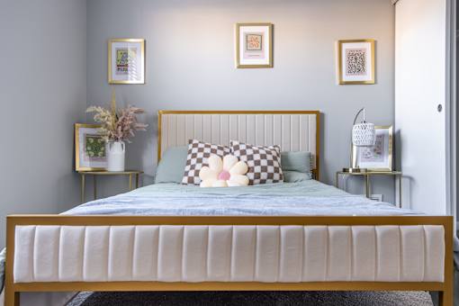 A bed with a white headboard and a blue bedspread with a checkered pillow in the middle.