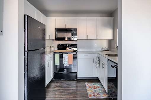 A black fridge and microwave in a kitchen with white cabinets.