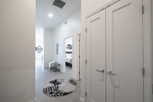 A hallway with a rug and a bedroom with a bed and a dresser.