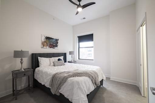 A bedroom with a bed, nightstand, and a ceiling fan.