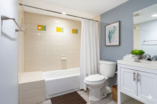 A white bathtub with a shower head and a white toilet in a bathroom.at Fernwood Grove Apartments, Tampa, FL