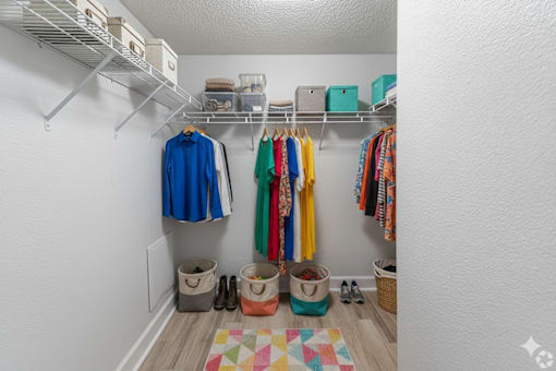 A white closet with clothes hanging and baskets underneath.