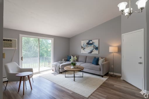 A living room with a white chair, a grey couch, a coffee table, and a painting on the wall.