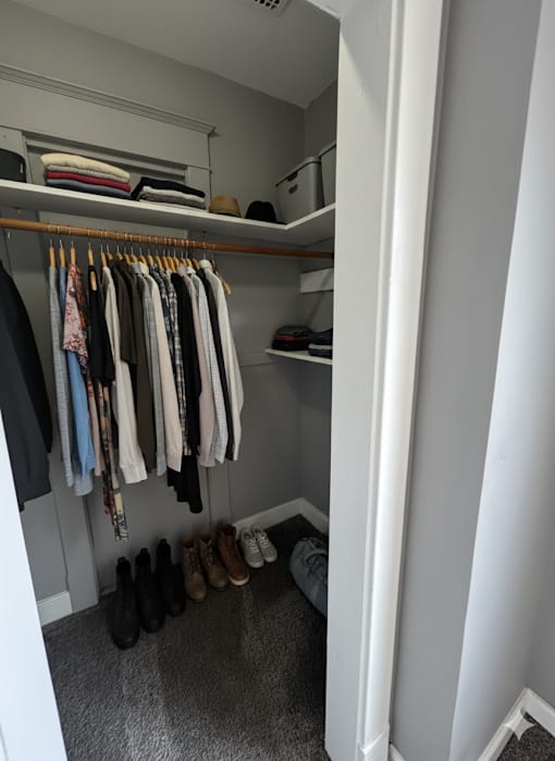 A small closet with clothes hanging and shoes on the floor.