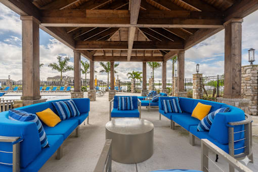 A wooden pavilion with blue couches and yellow pillows.