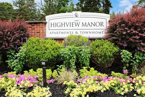 A sign for Highview Manor Apartments & Townhomes is surrounded by flowers.