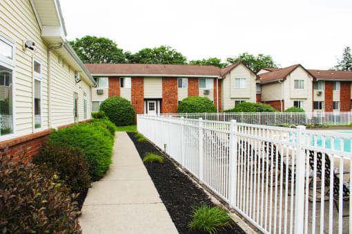 a white picket fence separates a sidewalk from a pool in an apartment complex