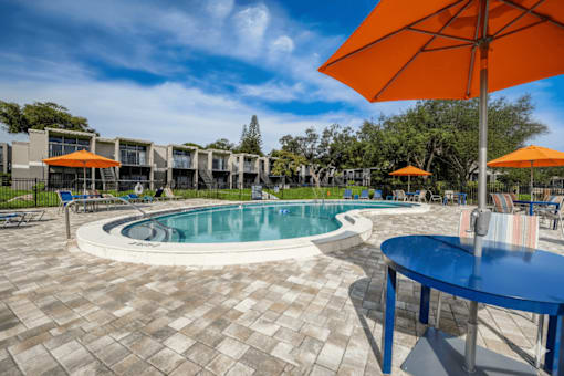 A round table with a blue tablecloth is in the foreground of a pool area.