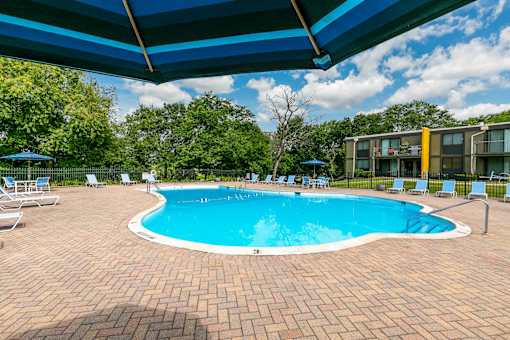 A swimming pool surrounded by a brick patio and lounge chairs under a blue canopy.