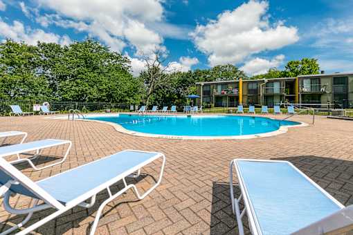 A pool surrounded by sun loungers and trees.