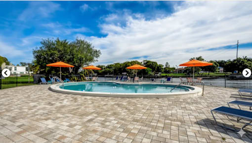 A round pool with a tiled floor and orange umbrellas in the background.