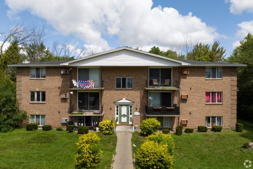 a brick apartment building with a green lawn and a flag on the balcony