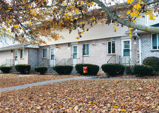 a brick house with a sidewalk in front of a tree with autumn leaves at Willowbrooke Apartments, Brockport, 14420
