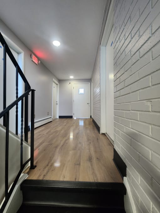 a long hallway with wood floors and white brick walls and a staircase