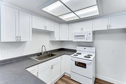 A white kitchen with a stove, sink, and cabinets.