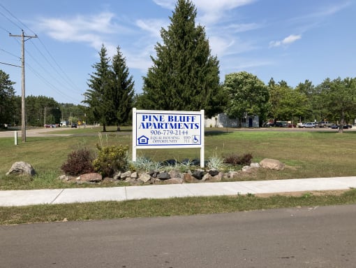 a sign in front of a grassy area with trees in the background