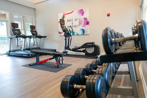 A gym with treadmills, elliptical machines, dumbbells, and a motivational poster.