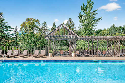 A pool with a wooden structure and chairs around it.