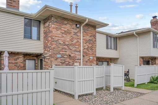 A white picket fence separates a house from a brick building.
