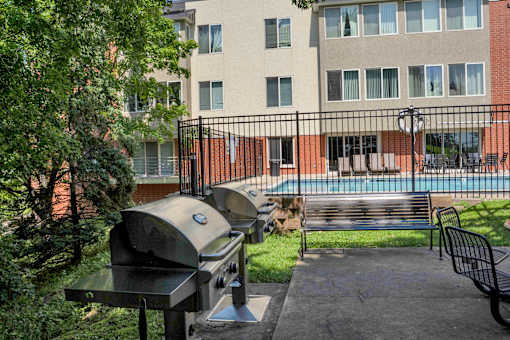 A BBQ grill is in the foreground of a courtyard with a pool and apartment building in the background.