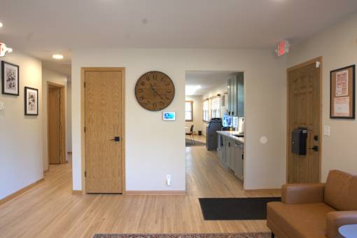 A hallway with a clock on the wall and a couch on the right side.