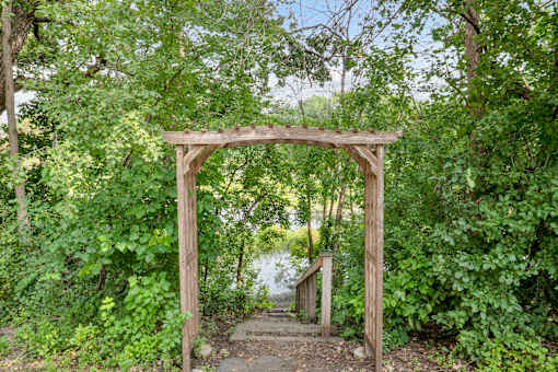 A wooden archway covered in greenery leads to a path.