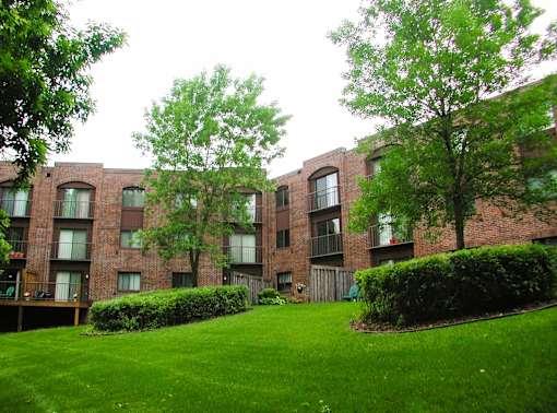 A grassy area in front of a brick building with trees and bushes.
