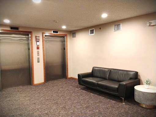A black leather couch sits in a room with a carpeted floor and two elevators.