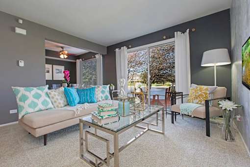 A living room with a glass coffee table and a couch with blue and white pillows.