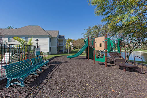A playground with a green slide and benches.