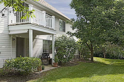 A white house with a balcony and a tree in front.