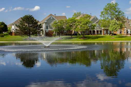 A fountain in the middle of a pond in front of a house.