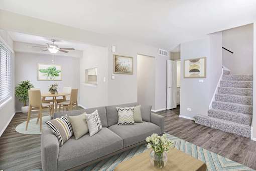 A living room with a grey couch, a wooden dining table, and a staircase.