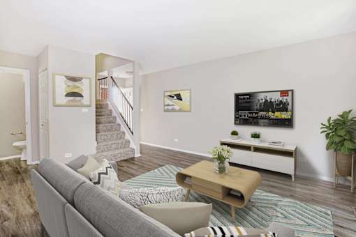 A living room with a grey couch, a wooden coffee table, and a staircase in the background.