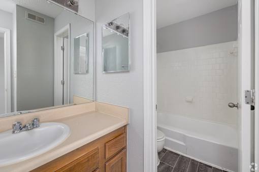 A white bathroom with a sink, mirror, and bathtub.
